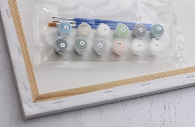 Puede incluir: Un kit de pintura por n&uacute;meros que incluye un lienzo, pinceles y 10 peque&ntilde;os frascos de pintura acr&iacute;lica. Los frascos de pintura est&aacute;n etiquetados con los n&uacute;meros del 1 al 10, y el lienzo es parcialmente visible en el fondo.