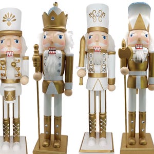 May include: Four decorative wooden nutcrackers in white and gold. Each figure has a unique design, including hats, uniforms, and accessories like a drum, sword, and axe. The nutcrackers stand on square bases.