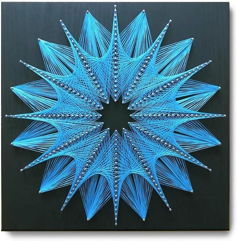 May include: A square black wooden board featuring a geometric string art design. Bright blue thread is wrapped around silver nails to create a complex, star-shaped pattern with multiple radiating points and a hollow centre, forming a symmetrical star.