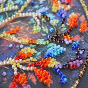 May include: Close-up of a beaded artwork with a vibrant floral design. The beads are in red, orange, yellow, blue, and green, with a gold border. The background is a dark, textured fabric.