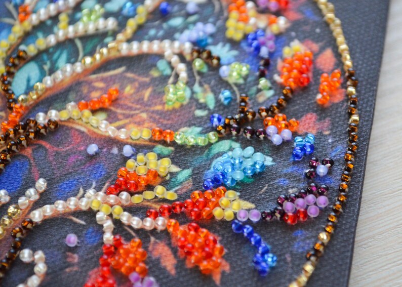 May include: Close-up of a beaded artwork with a vibrant floral design. The beads are in red, orange, yellow, blue, and green, with a gold border. The background is a dark, textured fabric.