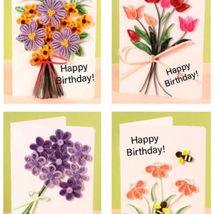 May include: Four handmade birthday cards with quilled paper flower designs. The cards feature bouquets of flowers in various colors, including purple, red, and orange, with the text "Happy Birthday!" on each card.