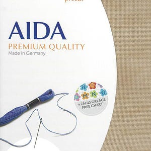 May include: A Zweigart precut Aida fabric package in a tan color. The packaging features the text AIDA PREMIUM QUALITY Made in Germany, a blue embroidery thread skein with a needle, and a circular graphic with the text +Z&Auml;HLVORLAGE FREE CHART.