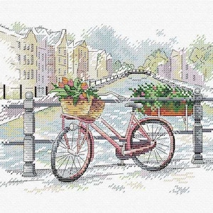 May include: A red bicycle with a basket of flowers is parked on a bridge over a canal. The bicycle is in front of a row of buildings with a blue sky in the background.