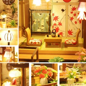 May include: A miniature dollhouse room with a Japanese theme. The room features a wooden floor, two chairs, a table, and a screen with a red and white floral pattern. There are also several light fixtures and a small potted plant.