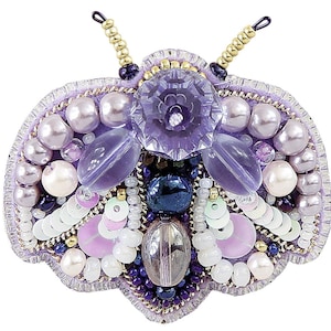 May include: A purple and white beaded brooch in the shape of a butterfly. The butterfly has a large, clear purple gem in the center and is surrounded by smaller purple and white beads.