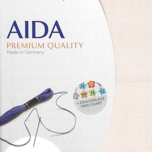 May include: Zweigart precut Aida premium quality fabric with a visible grid texture. The packaging features the text AIDA, PREMIUM QUALITY, Made in Germany, and a free chart icon. Includes a skein of purple embroidery floss and a needle, 16 ct.