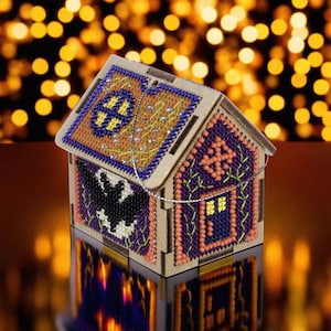 May include: A wooden house-shaped ornament with a beaded design. The front of the house features a purple and orange design with a small blue door. The top of the house has a beaded design with a black bat and a full moon.