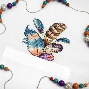 May include: A white fabric with a colorful embroidered design of feathers. A silver chain with colorful beads is draped over the fabric.