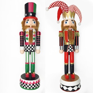 May include: Two decorative wooden nutcrackers. One wears a black, green, and red top hat and a uniform with a checkered pattern. The other wears a red and white jester hat and a red and black uniform with gold accents. Both have long, brown beards.