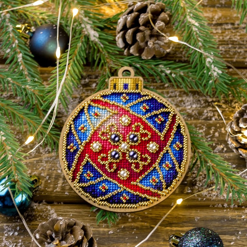 May include: A blue, red and gold Christmas bauble with a beaded design. The bauble is made of wood and is decorated with a variety of beads and sequins.