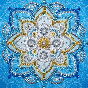 May include: A square fabric panel featuring a central mandala design meticulously embroidered with blue, silver, and gold beads. The intricate pattern consists of concentric floral layers, accented with small white pearls and clear glass beads.