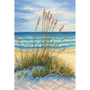 May include: A cross-stitch embroidery of a beach scene with tall, brown grass in the foreground and a blue ocean with white waves in the background.