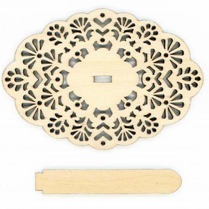 May include: A wooden cutout of a decorative oval with a delicate floral pattern. The oval has a small rectangular hole in the center. The cutout is accompanied by a separate wooden piece, a rectangular strip.