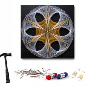 May include: A string art kit featuring a square black wooden board with a geometric star pattern created by white and gold threads wrapped around silver nails. The kit includes a black hammer, a pile of silver nails, two small spools of thread, and two metal wall hangers.