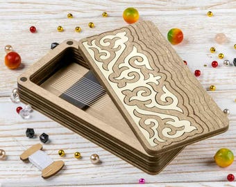 May include: A wooden box with an open lid, featuring an intricate cream-colored design on the lid. The box is light brown with a rectangular shape. The background includes decorative beads and small objects.