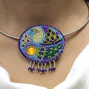 May include: A silver choker necklace with a round beaded pendant. The pendant is made of various colors of beads, including purple, blue, green, yellow, and gold. The pendant has a fringe of purple and gold beads.