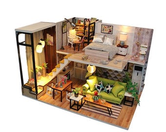 May include: A miniature dollhouse with a loft bedroom, a living room with a green sofa, and a dining area with a table and chairs. The dollhouse is made of wood and has a realistic design.