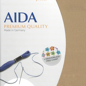 May include: A Zweigart precut Aida fabric in a tan color, measuring 48 x 53 cm or 19 x 21 inches. The packaging features blue text, a skein of blue embroidery thread, and a circular graphic with colorful flowers and the text + Z&Auml;HLVORLAGE FREE CHART.