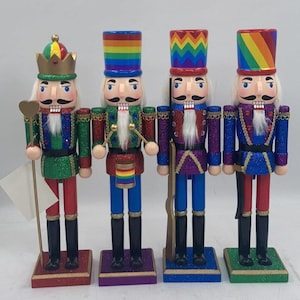 May include: Set of four wooden nutcracker figurines with rainbow-colored hats and glitter accents. The nutcrackers are dressed in different costumes, including a king, a drummer, a soldier, and a soldier.