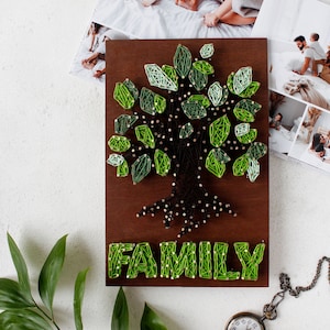 May include: A wooden wall hanging with a green string art tree and the word "FAMILY" underneath. The tree has a brown trunk and roots.