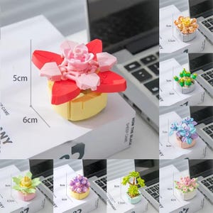 Peut inclure: Un ensemble de huit pots de fleurs miniatures en blocs de construction en plastique colorés. Chaque pot présente un motif de fleur différent, notamment une rose rose, une fleur jaune, un cactus vert, une fleur bleue, une fleur violette, un arbre vert, une fleur rose et une fleur jaune. Les pots mesurent environ 5 cm de diamètre et 6 cm de hauteur.
