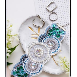 May include: A beaded bracelet kit with a white, blue, and green design. The kit includes 1,547 beads and is 6 inches by 2.36 inches. The kit is called "Arabesque" and has the code ADB-006.
