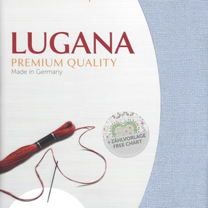 Peut inclure: Un tissu en toile Aida bleu clair pour point de croix, avec le texte "ZWEIGART precut LUGANA PREMIUM QUALITY Made in Germany" et "10/cm - 25 ct. 48 x 68 cm - 19" x 27" ". Un fil &agrave; broder rouge est enroul&eacute; autour d'une aiguille et un cercle avec le texte "+ Z&Auml;HLVORLAGE FREE CHART" se trouve dans le coin sup&eacute;rieur droit.