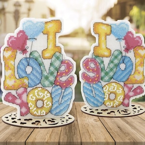 May include: Two wooden signs with the words "I love you" spelled out in colorful, patterned letters. The letters are arranged in a stack and are decorated with small, colorful balloons.