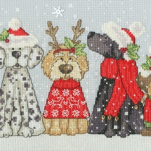 May include: A group of eight dogs wearing Santa hats and festive attire stand in a row against a snowy background. The dogs are all different breeds and sizes, and they are all looking at the camera.