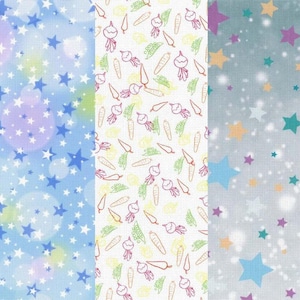 May include: Three fabric swatches with different patterns. The left swatch is light blue with white stars and a gradient of light purple and yellow. The middle swatch is white with a repeating pattern of carrots, turnips, and green leaves. The right swatch is light grey with a repeating pattern of stars in various colours, including orange, purple, teal, and blue.