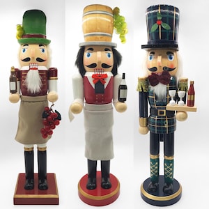 May include: Three wooden nutcracker figures standing on circular bases. The left figure wears a green hat and apron, holding a bottle and grapes. The centre figure wears a barrel hat, holding a bottle. The right figure wears a plaid hat, holding a tray.