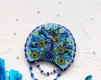 May include: A beaded peacock brooch with blue, green, and gold beads. The brooch has a chain of blue beads hanging from the bottom.