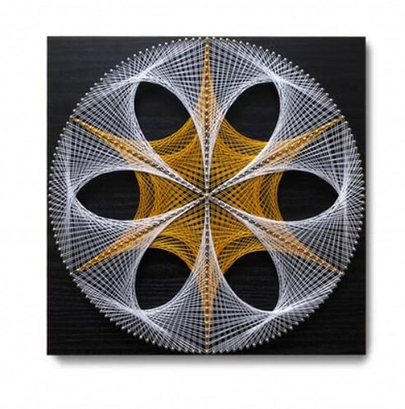 May include: A square string art piece on a black wooden board featuring a circular geometric pattern. The design is created with white and gold threads wrapped around silver nails, forming a central six-pointed star and outer petal shapes.