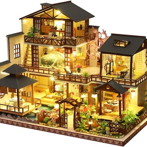 May include: A multi-level dollhouse with a wooden frame and a light brown roof. The dollhouse has a balcony, windows, and a garden with flowers and trees. The dollhouse is lit up with small lights.