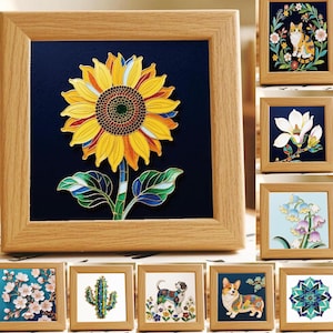 May include: A square wooden frame containing a stained glass-style sunflower art piece with yellow petals, a dark center, and green leaves against a deep blue background. The collection includes other framed designs featuring a cat, flowers, a cactus, and dogs.