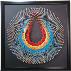 May include: A square black frame containing string art on a black background. The artwork features a circular arrangement of silver nails connected by vibrant red, yellow, and bright blue threads, creating a central teardrop-shaped negative space.