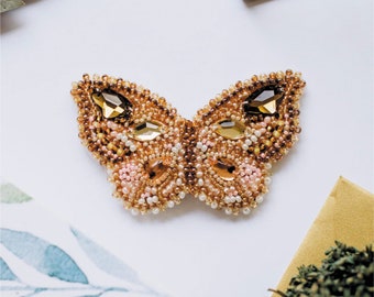 May include: A delicate butterfly brooch made of beads and rhinestones in shades of brown, pink, and gold. The butterfly has a detailed design with intricate beadwork and sparkling rhinestones.