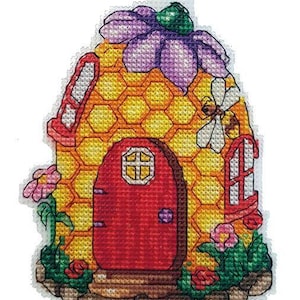 May include: A yellow and red beehive-shaped house with a purple flower on top. The house has a red door with a small window and a yellow honeycomb pattern. There are green plants and pink flowers around the base of the house.
