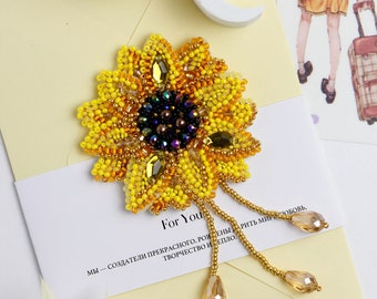 May include: A beaded sunflower brooch with a yellow and orange center and a dark brown center. The brooch has three strands of beads hanging from the bottom.