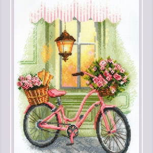 May include: A pink bicycle with a basket of flowers and bread in front of a window with a lantern hanging above. The window has a striped awning and the scene is set against a green wall.