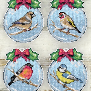 May include: Four cross-stitch ornaments featuring colorful birds perched on branches within blue spheres. Each ornament is topped with a red bow and green holly. The birds include a finch, goldfinch, bullfinch, and blue tit.