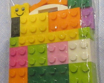 May include: A plastic bag filled with colorful Lego blocks. The blocks are various shapes and sizes, including a yellow block with a smiley face.