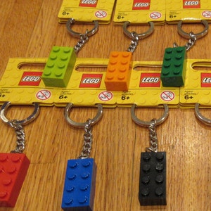 May include: A set of six LEGO keychains featuring different colored LEGO bricks. Each keychain has a silver chain and a yellow card with the LEGO logo and the text "Ages/ edades 6+".