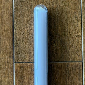 以下が含まれることがあります： 透明で丸みを帯びた上部が付いた、円筒形の水色の物体。物体は茶色の木製の表面に対して垂直に配置されています。物体はライトまたは照明器具の一部のように見えます。