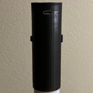 以下が含まれることがあります： 白いライトセーバーの柄にある黒い充電ポートのクローズアップ。