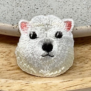 May include: White embroidered patch of a polar bear's face with pink ears and black eyes.