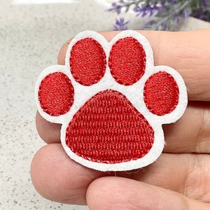 May include: Red felt paw print applique with white stitching. The paw print is approximately 5 cm in diameter.