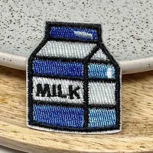 Peut inclure: Un patch thermocollant brodé en bleu et blanc en forme de brique de lait avec le mot "MILK" imprimé sur le devant.