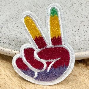 May include: A colorful peace sign patch with a white outline. The patch is embroidered with red, yellow, and green thread.